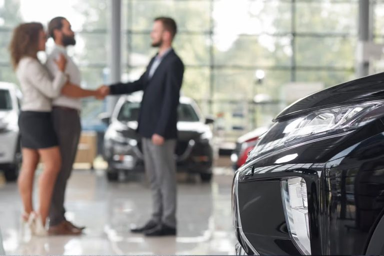 Car buyer and dealership representative shaking hands in a showroom with a vehicle in the foreground